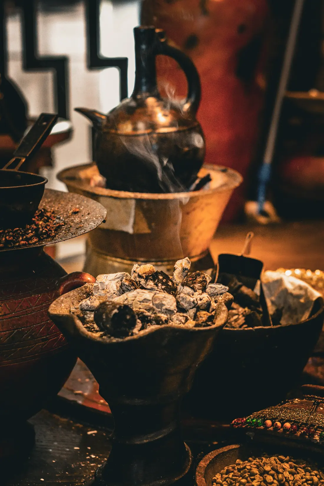 A jebena on a stand above smoking incense and roasted beans