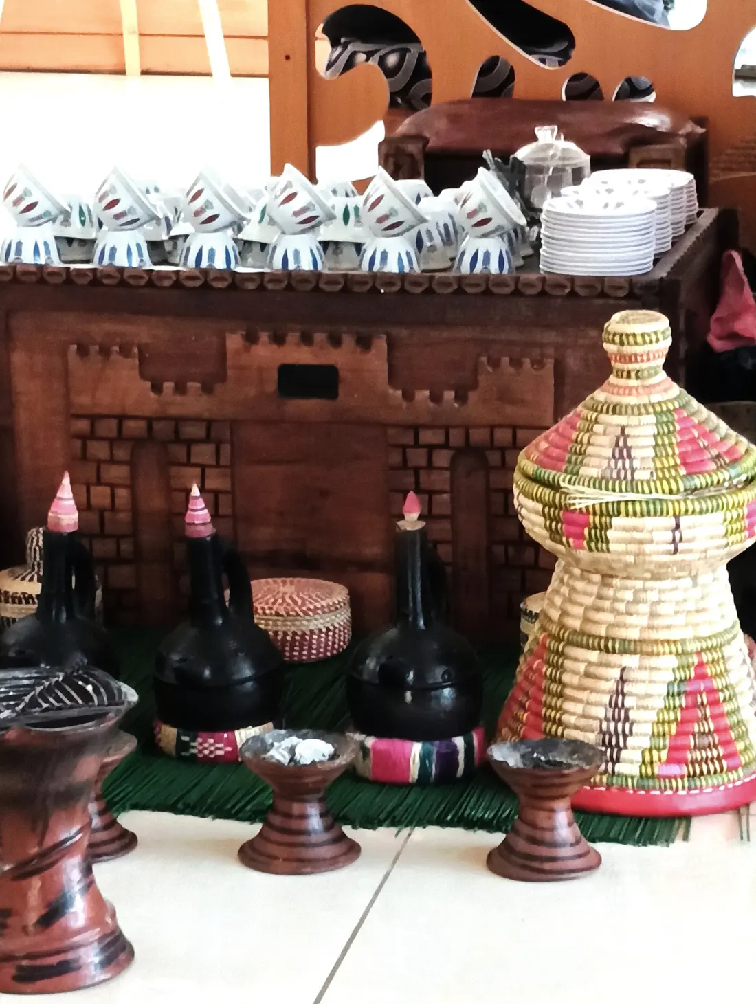 Jebena pots, small cups and a tall woven basket set out for an Ethiopian coffee ceremony